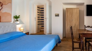 Una camera da letto con un letto, un comodino con lampada, una pianta in vaso, un armadio in legno e un'area pranzo con tavolo e sedie.