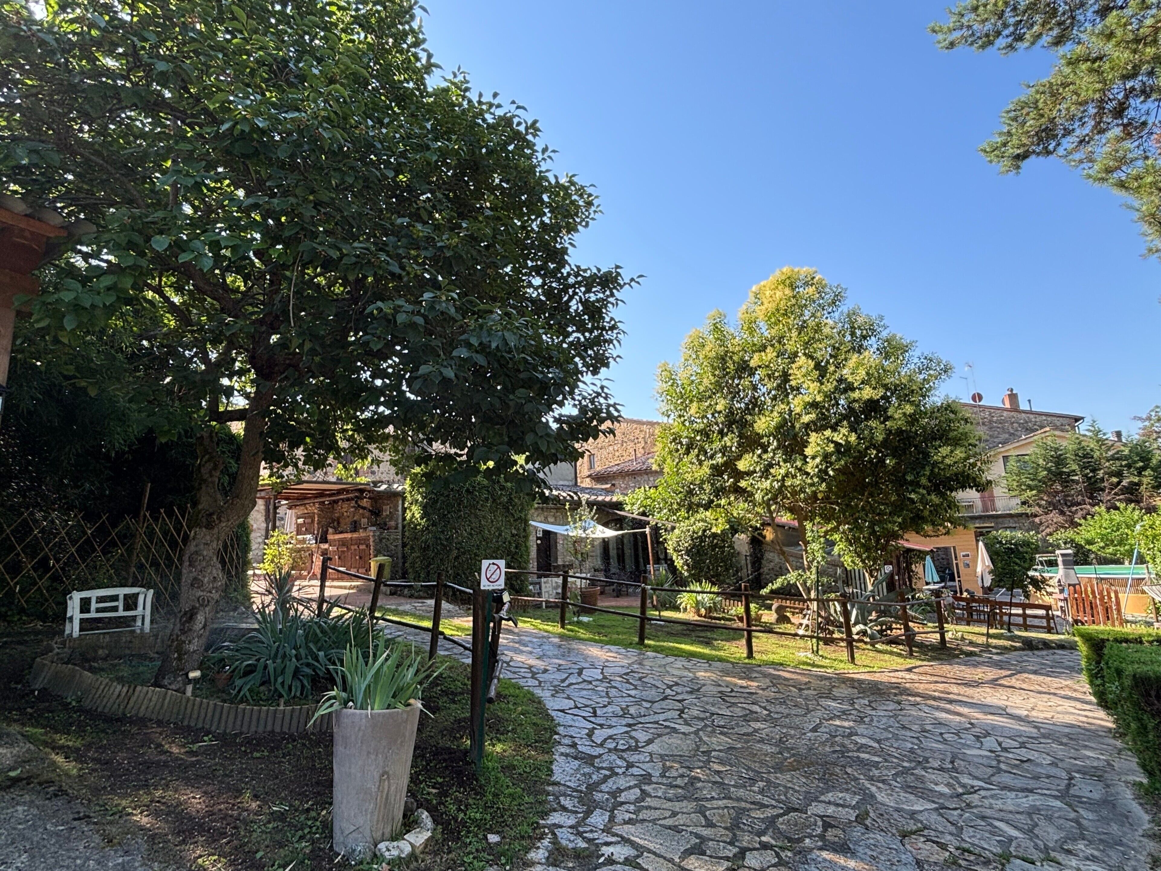 A stone pathway leading to a rustic building with a wooden fence and greenery.