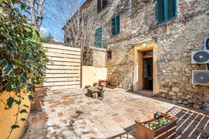 Un bâtiment en pierre avec un portail en bois, un petit espace extérieur aménagé avec des sièges et une porte donnant sur l’intérieur.