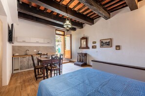 Une pièce comprenant un lit, un plancher en bois, une table à manger avec des chaises, un coin cuisine avec des placards, un plafond en bois et une fenêtre.
