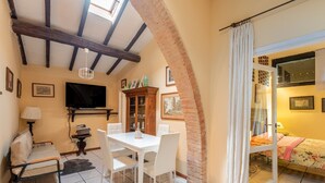 A room with a dining table, chairs, a TV, a cabinet, and a bed with a curtain. - Apartment 'Glicine - Antiche Dimore' with Shared Pool, Wi-Fi, and Air Conditioning (Siena)