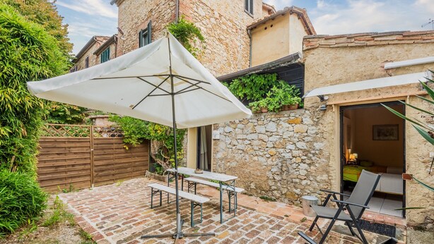 A patio with a table and chairs, a white umbrella, and a stone wall. - Apartment 'Glicine - Antiche Dimore' with Shared Pool, Wi-Fi, and Air Conditioning (Siena)