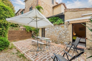 Un patio con una mesa y sillas, una sombrilla blanca y un muro de piedra.