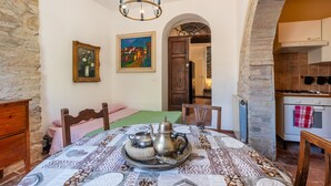 Un coin repas avec une table dressée pour deux personnes, un lustre, un tableau et une vue sur la cuisine.