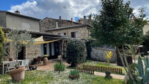 Un bâtiment rustique en pierre, doté d’une terrasse, de sièges extérieurs et d’un jardin agrémenté de diverses plantes et fleurs.