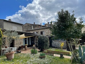 Ein rustikales Steinhaus mit Terrasse, Sitzgelegenheiten im Freien und einem Garten mit verschiedenen Pflanzen und Blumen.