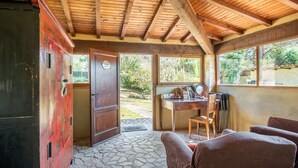 Un chalet rustique doté d’un sol en pierre, de poutres en bois au plafond, d’un bureau avec une chaise et d’une grande fenêtre donnant sur la verdure.
