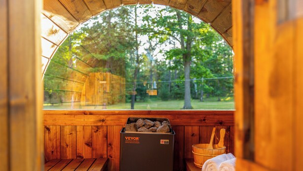 A wooden sauna with a bench, a stone heater, and a wooden bucket.