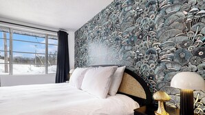A bedroom with a large bed, a nightstand, a lamp, and a wall with a detailed floral pattern.