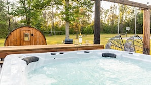 A hot tub with a wooden deck, a wooden barrel, and a basketball hoop in a wooded area.