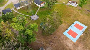 An aerial view of a property with a central circular patio, a tennis court, and surrounding buildings.