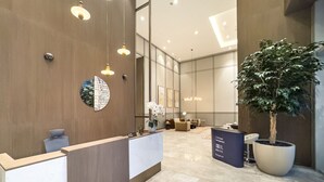 Un área de recepción moderna con un mostrador de recepción, una planta grande en maceta y un espacio de estar con sofás.