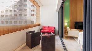 Ein Balkon mit Korbmöbeln, einem roten Sofa und einem Fernseher in einem Raum mit grünen und Holzwänden.