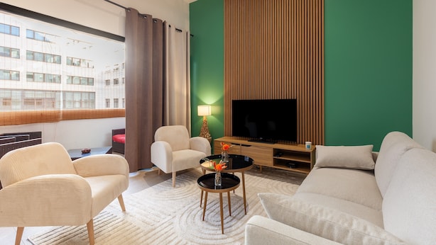 Ein modernes Wohnzimmer mit einer Couch, Sesseln, einem Couchtisch und einem Fernseher an einer grünen Wand.