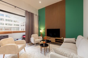 A modern living room with a sofa, armchairs, a coffee table, and a TV against a green wall. - Apartment 'Le Castel' with Private Terrace and Wi-Fi (Marseille)