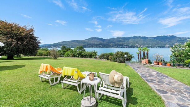 Un jardín con mesas al aire libre y vistas a un lago y montañas.