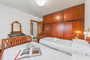 A hotel room with two single beds, a wooden wardrobe, a wooden chair, a wooden desk, and a mirror.