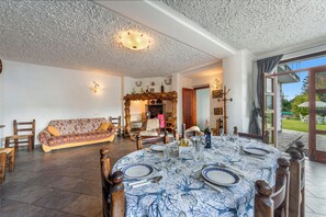 A dining area with a round table set for four, a sofa in the background, and a view through an open door to the outdoors.