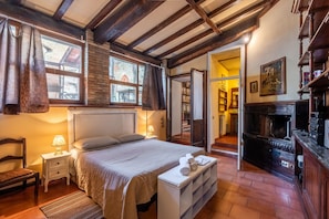 Une pièce confortable avec un lit, une table de chevet avec une lampe, un banc avec des serviettes, une cheminée et un plafond en bois.