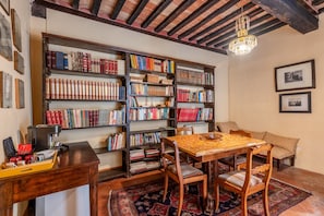 A library with bookshelves, a wooden table, chairs, a coffee machine, and a patterned rug.