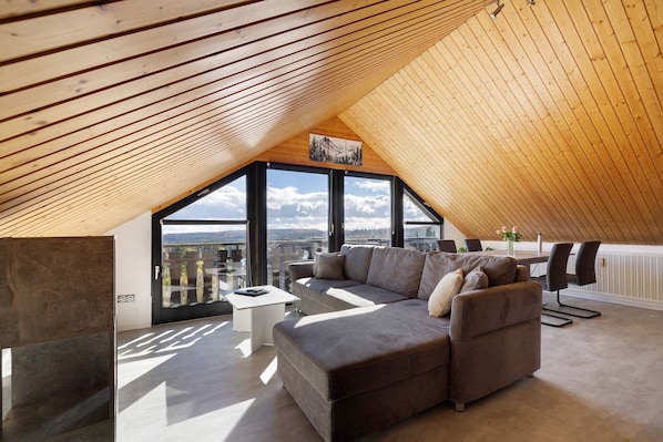 Une chambre de style loft moderne, avec un plafond en pente, de grandes fenêtres, un canapé, une table basse et une vue sur l’extérieur.