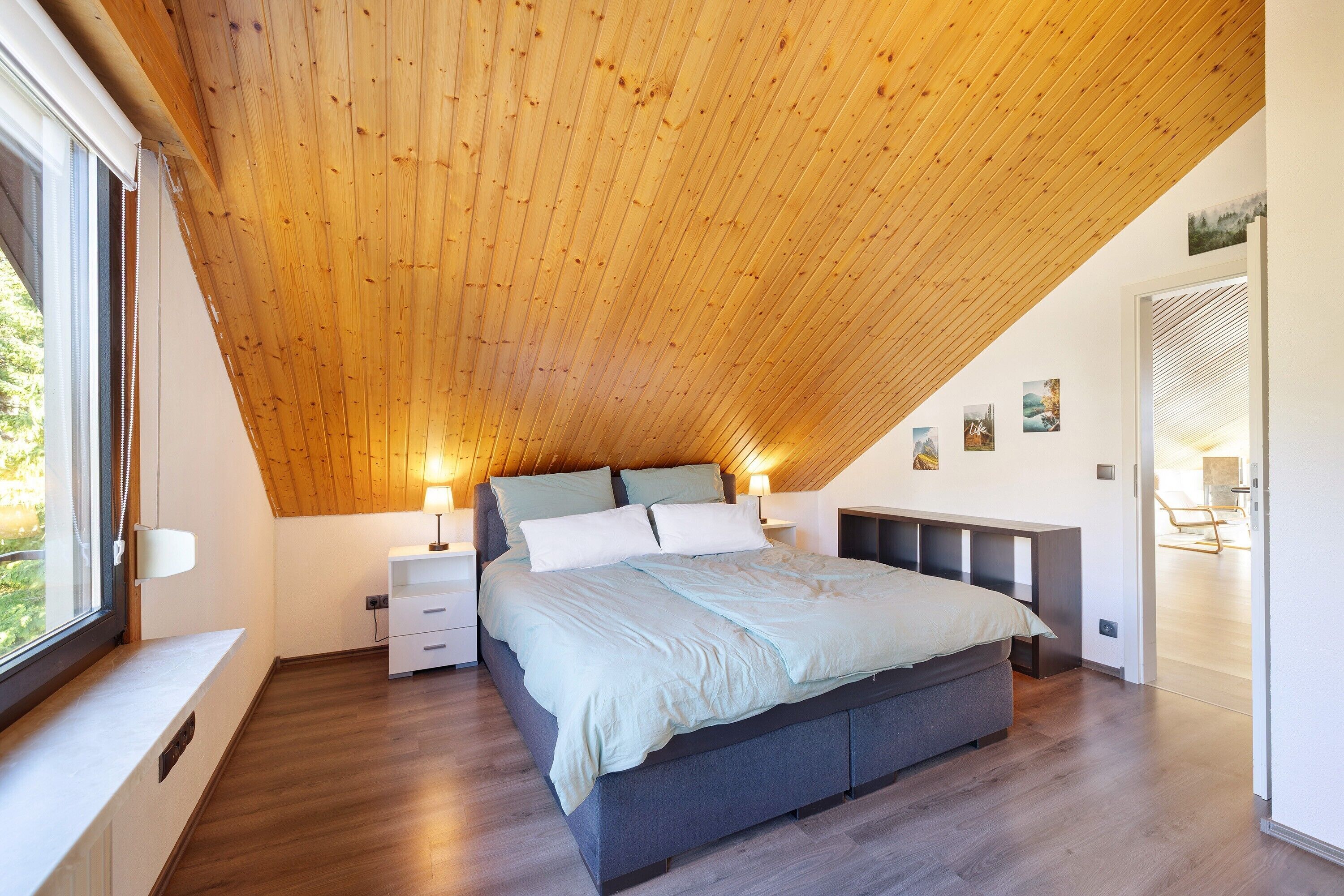 A bedroom with a sloped ceiling, a bed, bedside tables, and artwork on the walls.