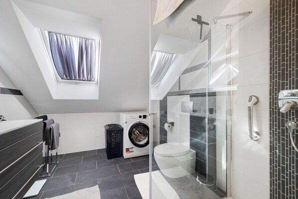 A modern bathroom with a washing machine, a toilet, and a glass-enclosed shower.