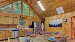 Una cabaña de madera con una gran mesa de comedor dispuesta para cuatro, armarios de madera, un refrigerador y un reloj en la pared.