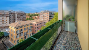 A balcony with a view of surrounding buildings, a green planter, and a patterned floor. - Emilia Suite Garden (Modena)
