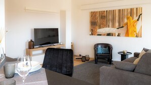 A modern living room with a flat-screen TV, a large abstract painting, a leather armchair, and a grey sofa. - Emilia Suite Garden (Modena)