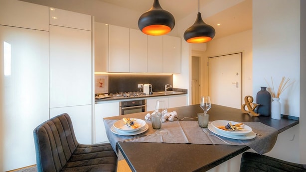 A modern kitchen with white cabinets, a central island with a dark countertop, and two pendant lights. - Emilia Suite Garden (Modena)