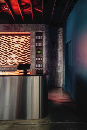 A reception area with a modern design, including a patterned wall, a counter, and a shelving unit with bottles. - Hotel Hilo - Room 101 (Louisville)