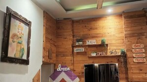 Une pièce aux murs recouverts de lambris en bois, avec un ventilateur de plafond, un tableau encadré, une pancarte indiquant « BUREAU DE MADAME », une fenêtre avec des rideaux et une table avec une chaise.
