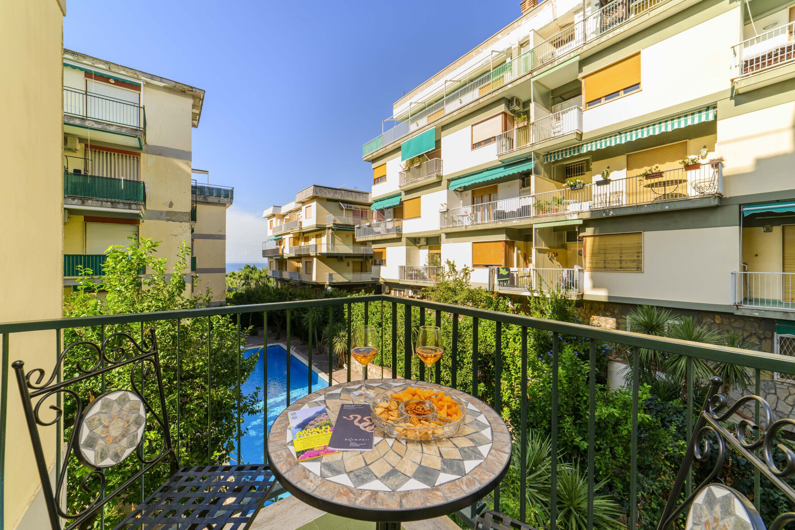 A balcony with a pool view, a table with snacks and drinks, and a book.