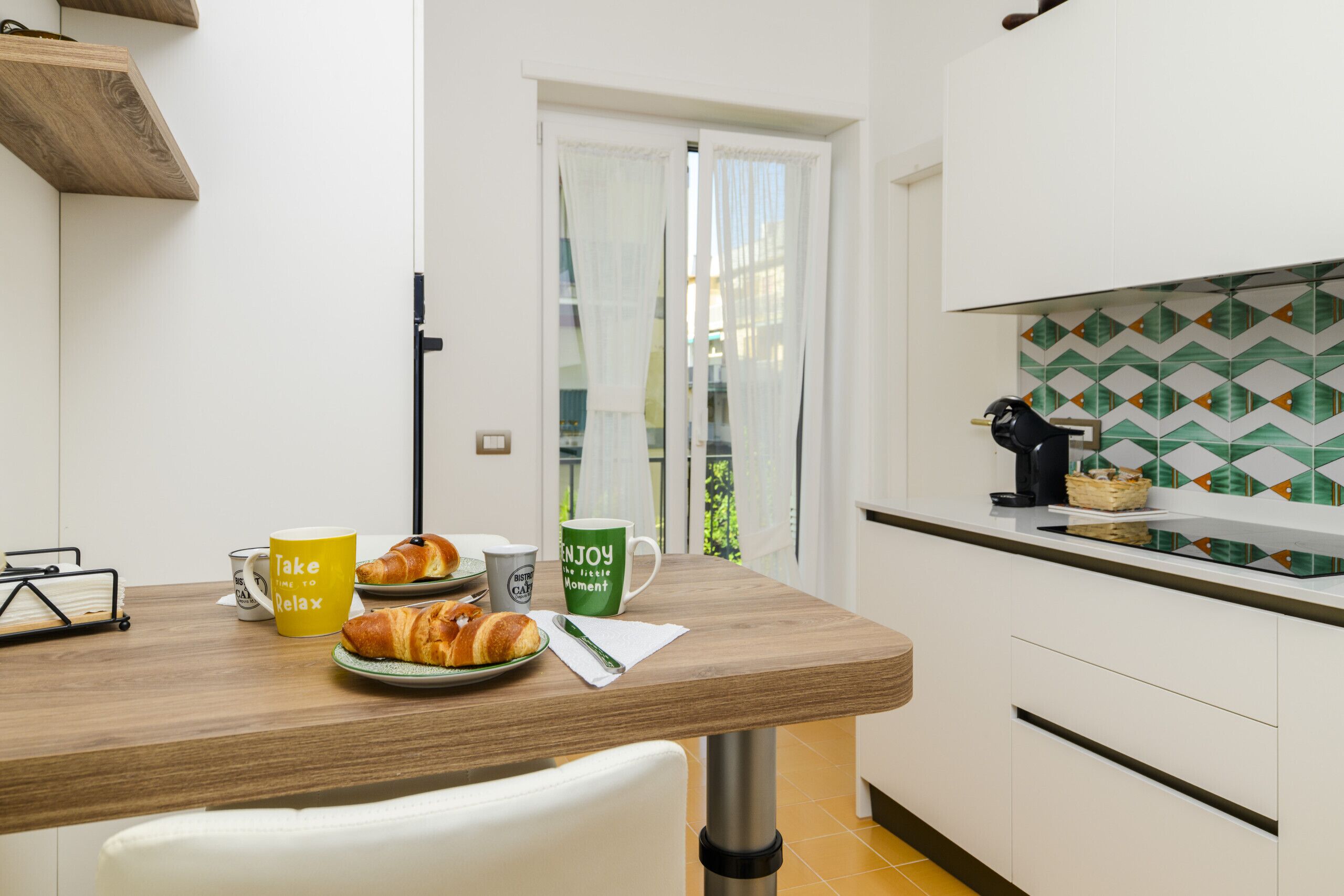 Une cuisine avec un plan de travail en bois, une chaise blanche et une porte donnant sur un balcon.