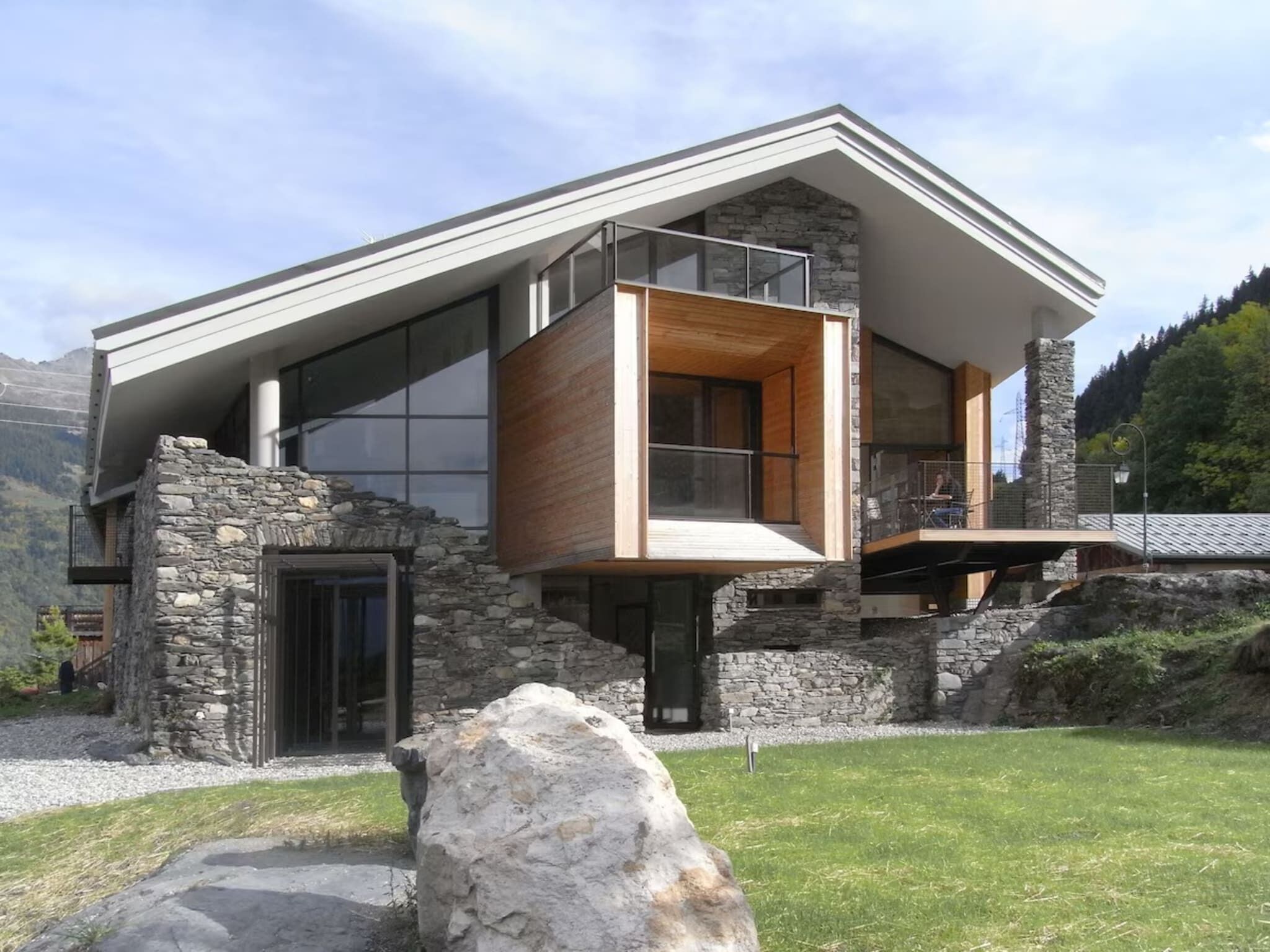 Ein modernes Haus mit einer Natursteinfassade, großen Fenstern und einem Holzbalkon.