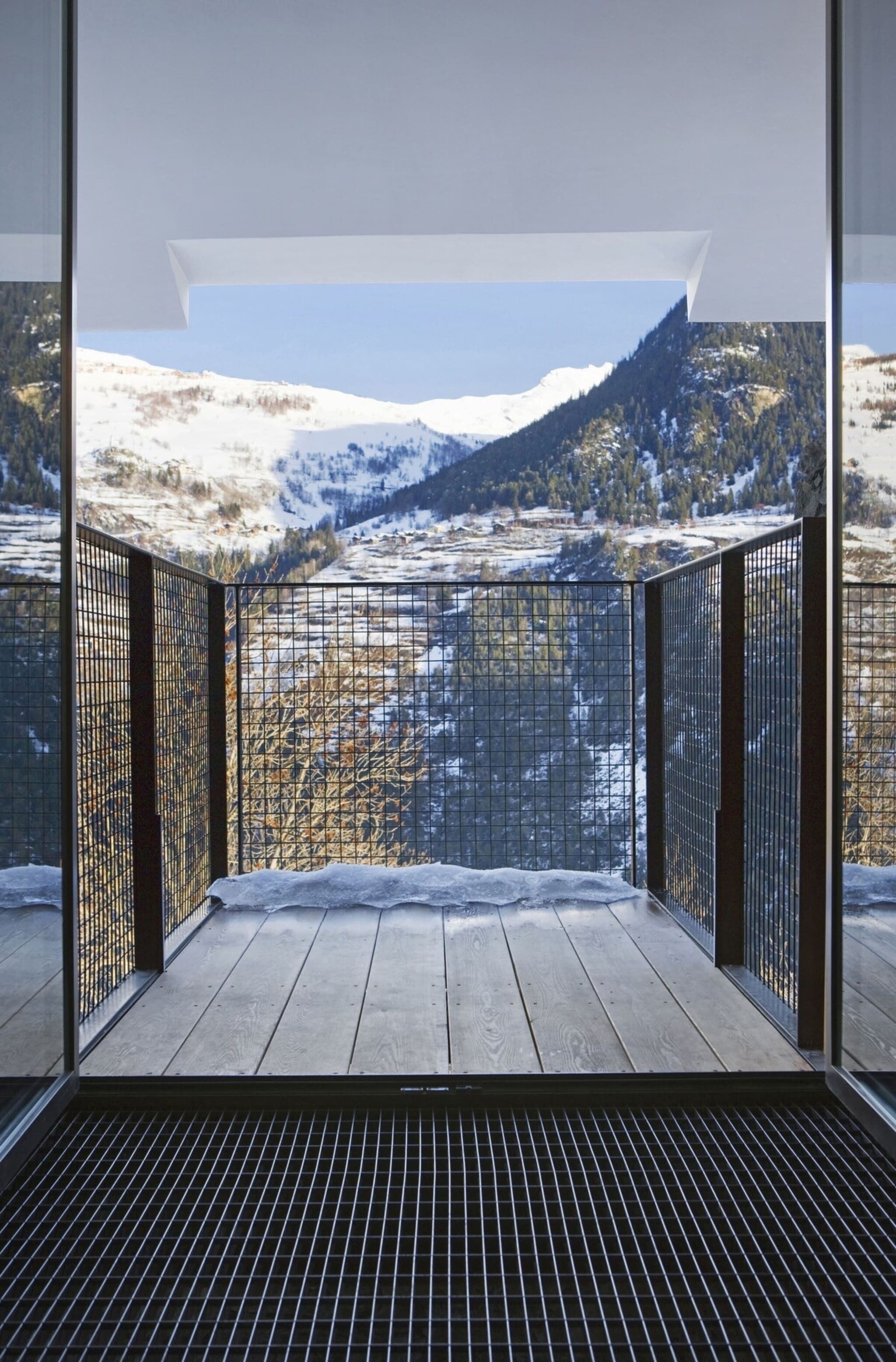 A balcony with a metal railing, a wooden floor, and a view of snow-covered mountains.