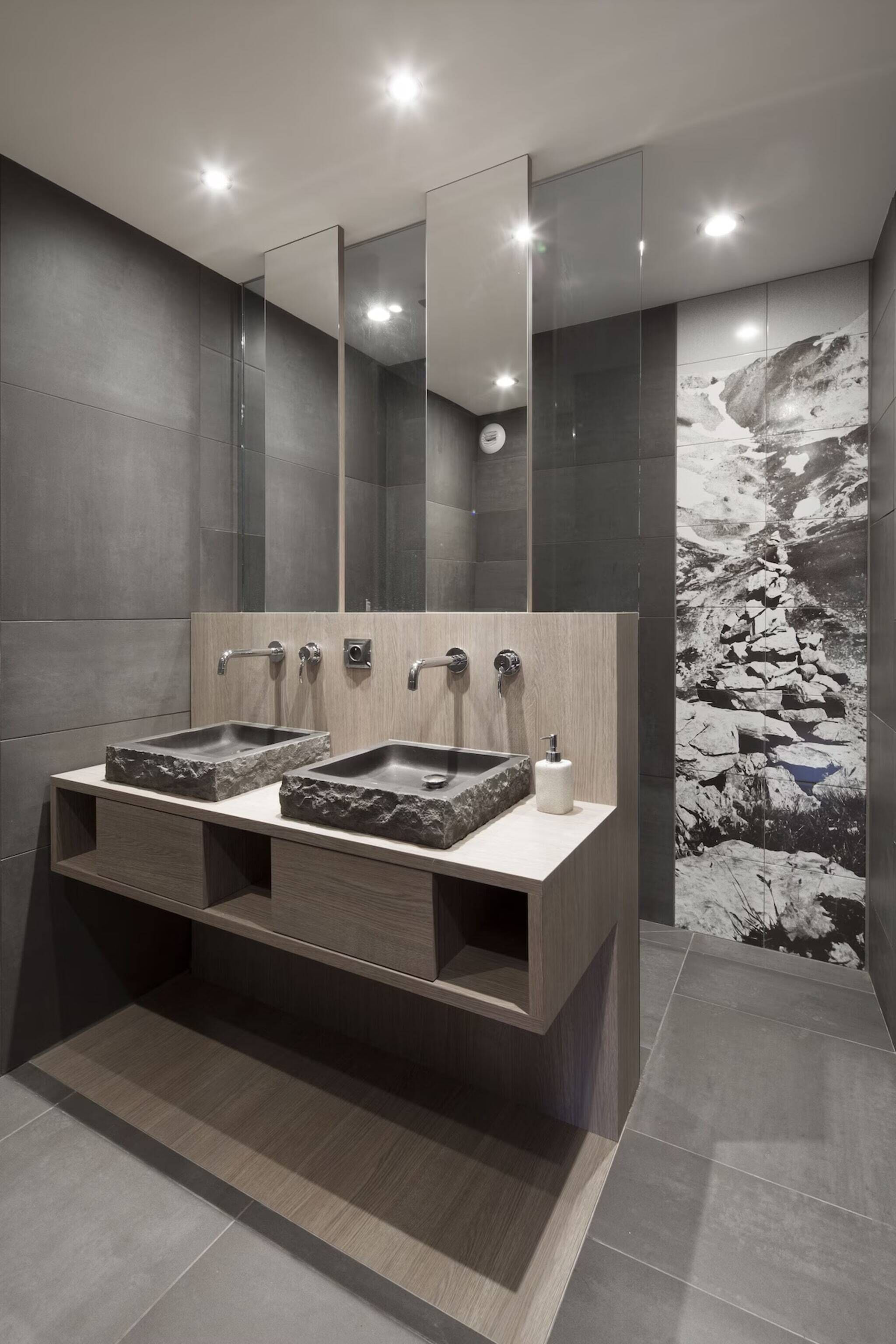 Un baño moderno con dos lavabos, un espejo grande y un mural de piedra en la pared.