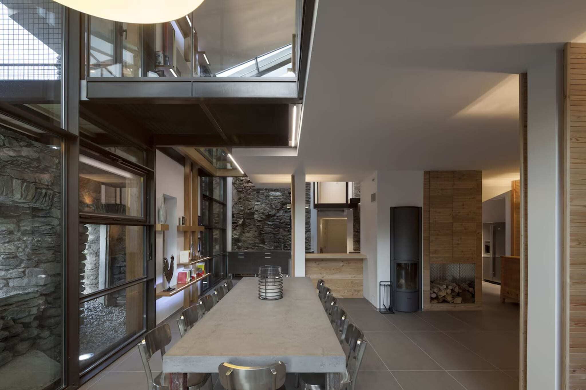 Een moderne eethoek met een lange tafel, stenen muren en een open haard.