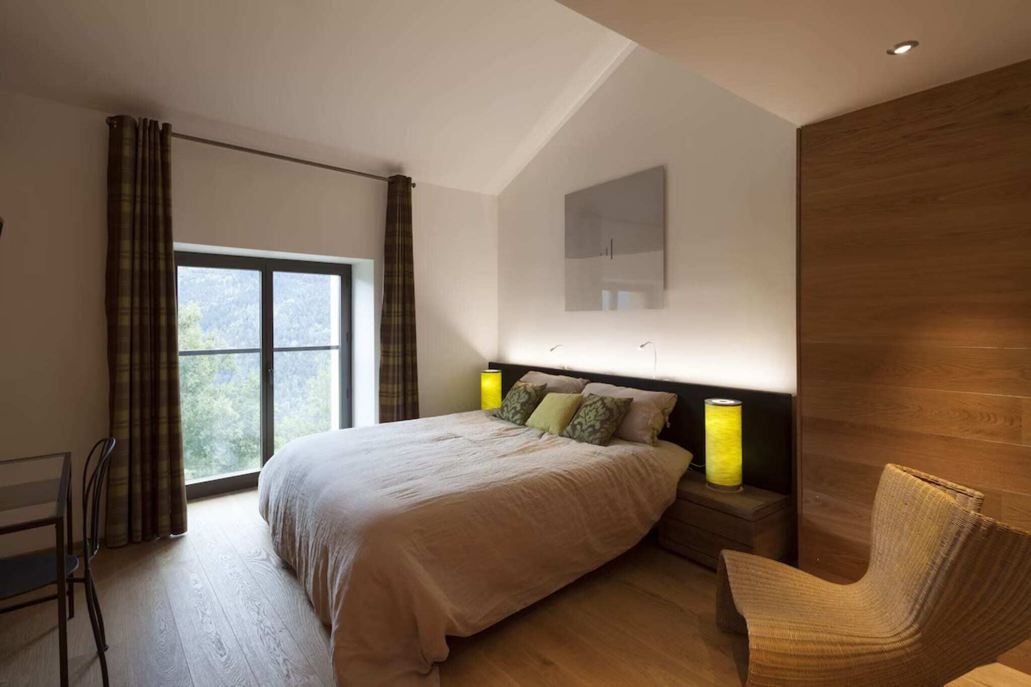 Un dormitorio moderno con una cama grande, lámparas de noche, una silla y vistas por la ventana.