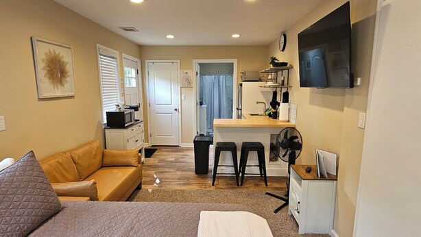 A compact hotel room with a bed, a sofa, a desk with a chair, a TV, and a small kitchenette. - South Shore Studio in Mastic (Mastic)