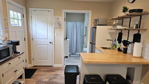 A compact kitchen with a microwave, coffee maker, and a refrigerator. There are two black stools and a trash bin. - South Shore Studio in Mastic (Mastic)