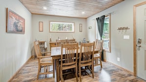 A dining area with a wooden table and chairs, a window with a view of greenery, and a door with a coat rack. - Summit Lodge (Fairplay)