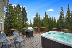 Ett trädäck med ett bubbelbad, en grill och Adirondack-stolar.