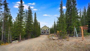 A house surrounded by tall trees with a dirt path leading to it. - Summit Lodge (Fairplay)