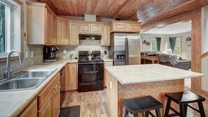 A kitchen with wooden cabinets, a stainless steel sink, a black stove, and a refrigerator. - Summit Lodge (Fairplay)