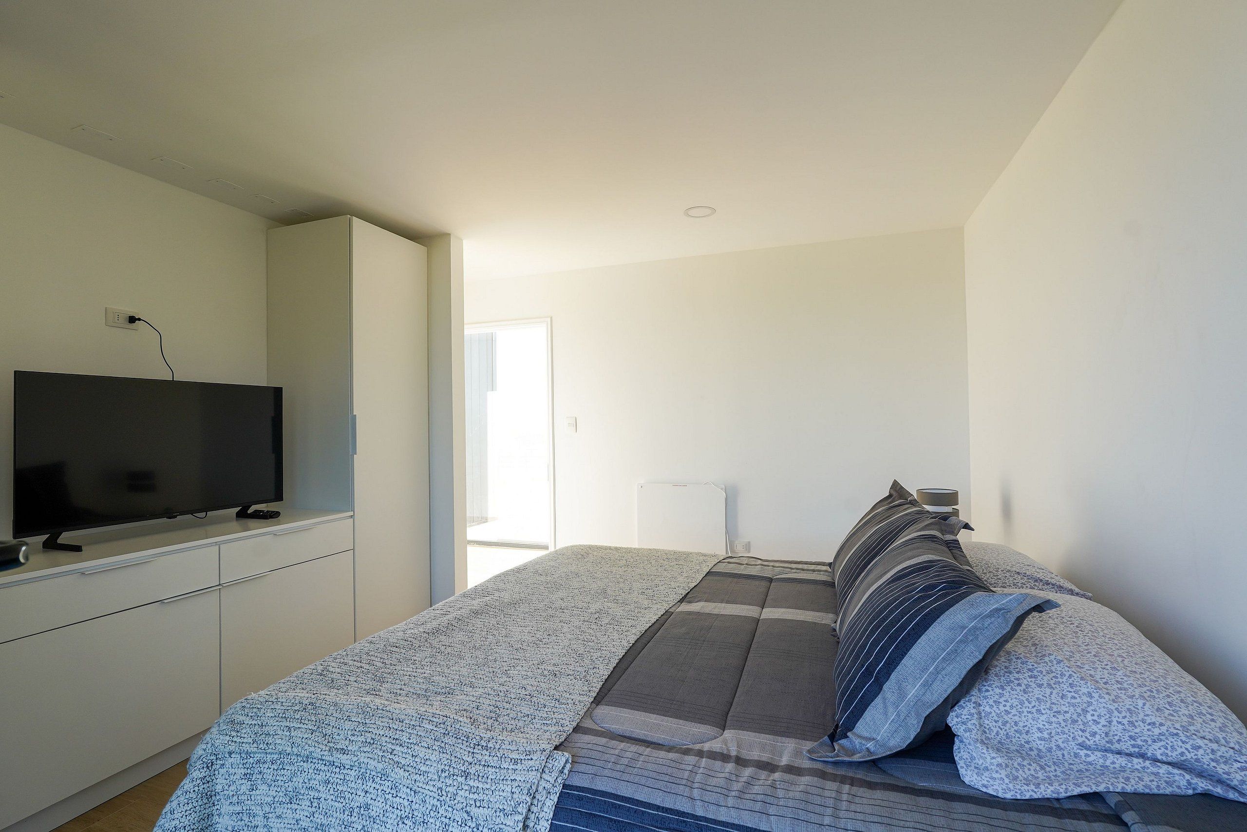 A bedroom with a bed, a TV on a stand, and a window.