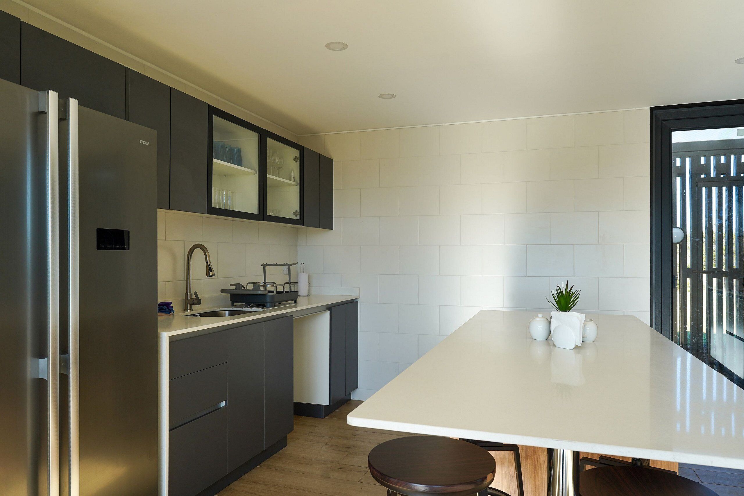 Eine moderne Küche mit integriertem Kühlschrank, dunklen Schränken, einer weißen Arbeitsplatte und einer kleinen Pflanze auf der Kochinsel.
