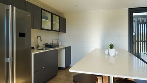 A modern kitchen with a built-in refrigerator, dark cabinetry, a white countertop, and a small plant on the island. - Oceana Suites Las Tranqueras (Puerto Varas)