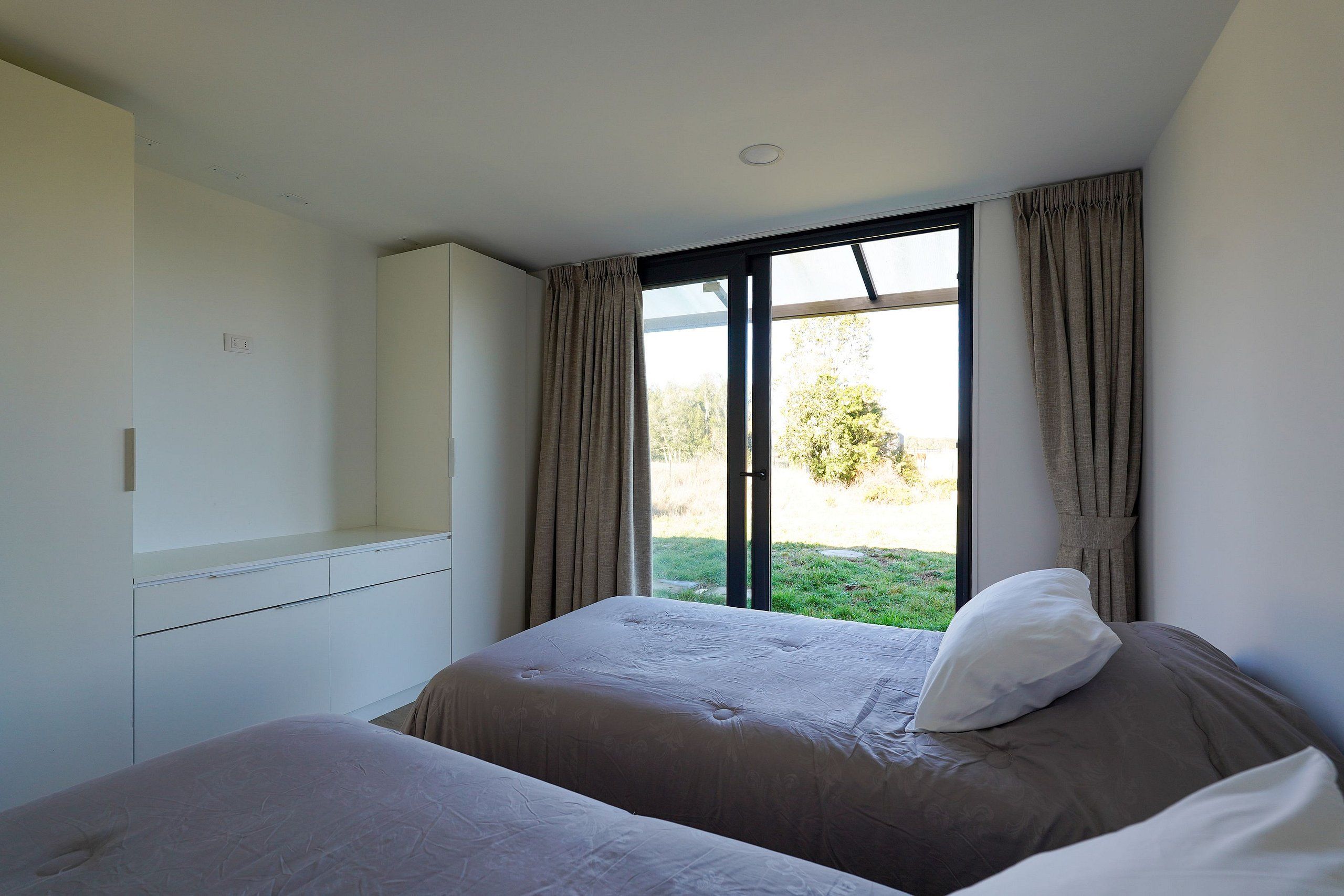 A bedroom with two beds, a wardrobe, and a large window with curtains.